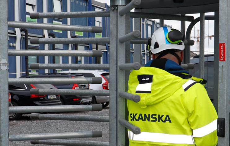 En person i neongul varseljacka och skyddshjälm går igenom ett vändkors vid en byggarbetsplats.